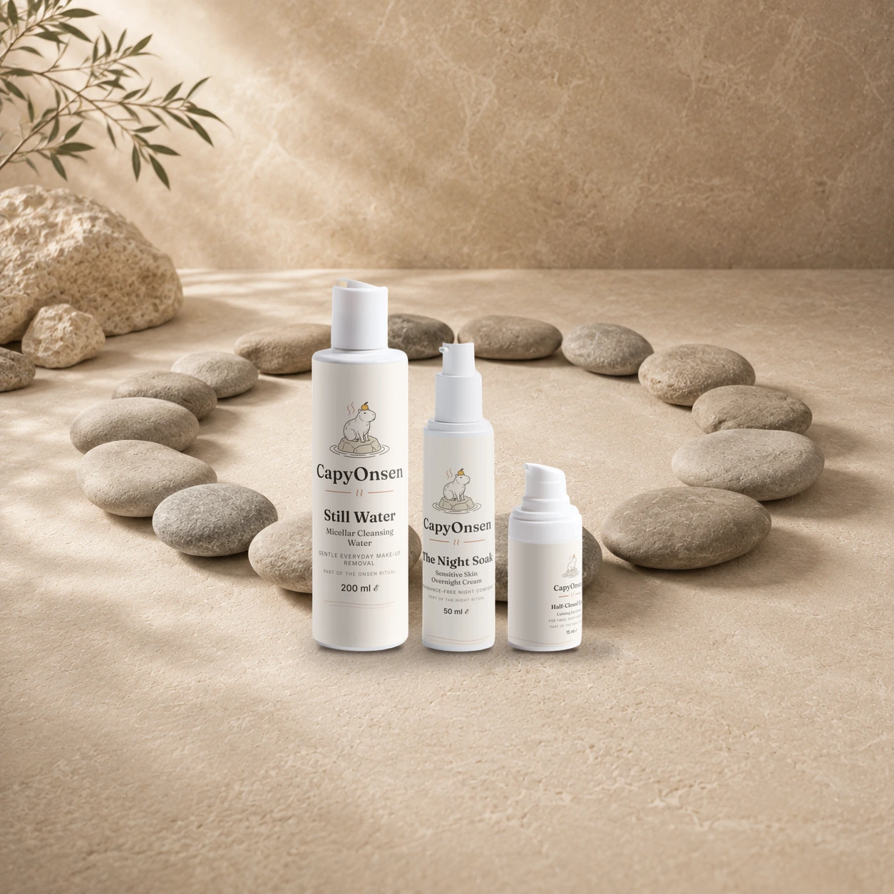 CapyOnsen Night Ritual Set: Micellar Cleansing Water (200ml), Sensitive Skin Overnight Cream (50ml) and Calming Eye Cream (15ml) bottles arranged inside a ring of smooth stones